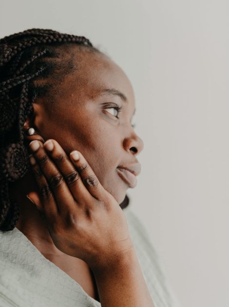 Close-up profile portrait of a woman gently touching her cheek, showcasing radiant skin