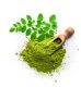 Overhead view of Matcha tea powder heap and Moringa leaves isolated on white background. A wooden serving scoop complete the composition. High resolution 42Mp studio digital capture taken with Sony A7rII and Sony FE 90mm f2.8 macro G OSS lens